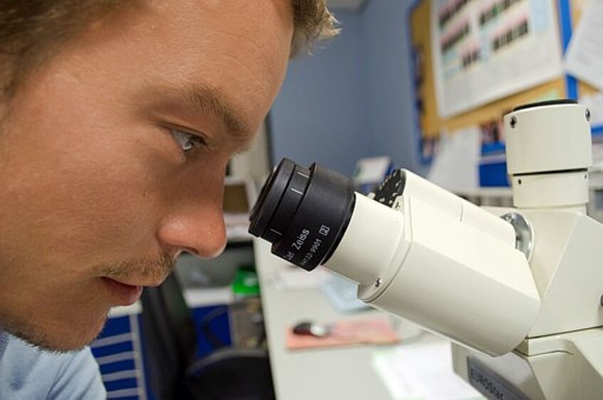 Mann, der in ein Mikroskop schaut